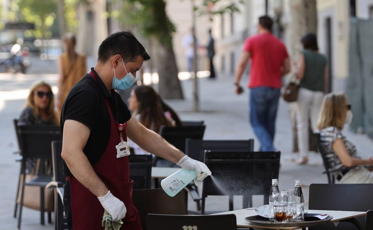 Un camarero desinfecta la mesa de una terraza.