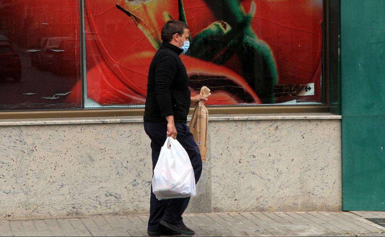 Un hombre con la mascarilla puesta lleva las bolsas de la compra por una calle de Cantalejo. 