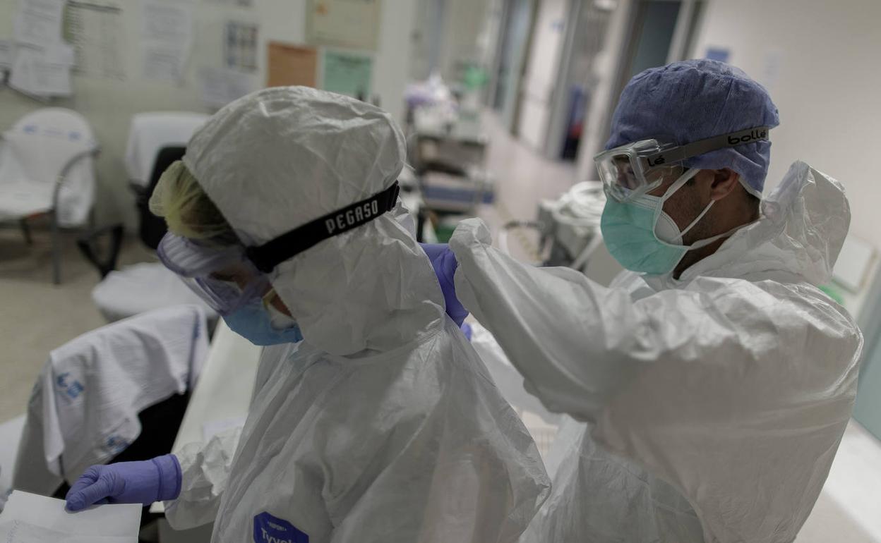 Un sanitario ayuda a una compañera a ponerse el traje de protección. 