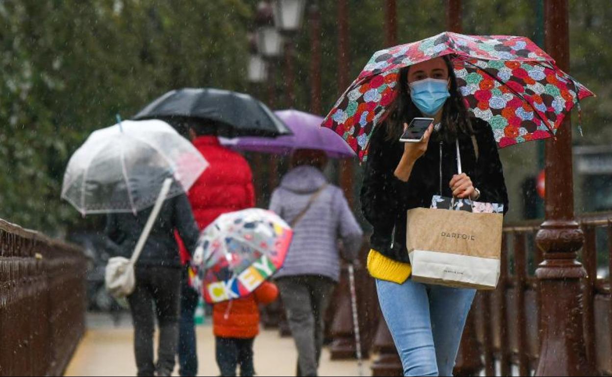 Los viandantes se protegen de la lluvia en el Puente Mayor.
