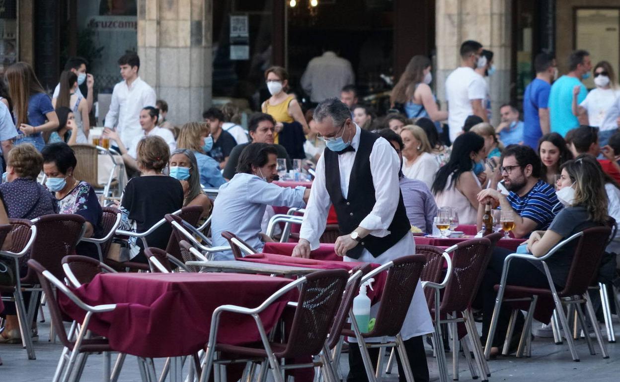 Un camarero desinfecta las mesas de una terraza de un restaurante en Salamanca.