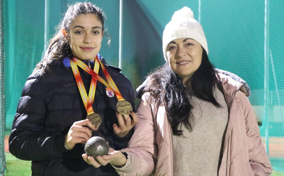 Fiona Villarroel y Margarita Ramos posan con un peso y las dos medallas de oro logradas por la primera en los campeonatos de España de atletismo sub-16 de este año 2020.