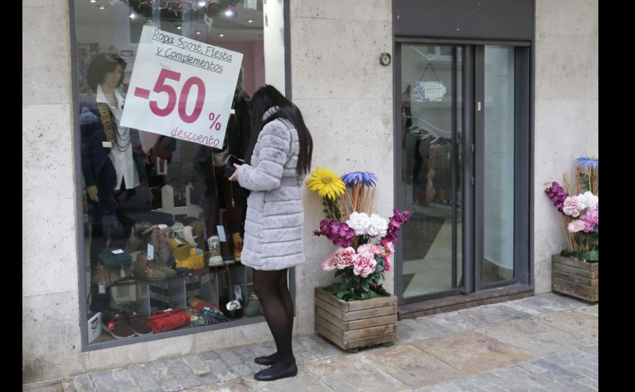 Una mujer observa el escaparate de un comercio que ofrece descuentos en sus productos. 