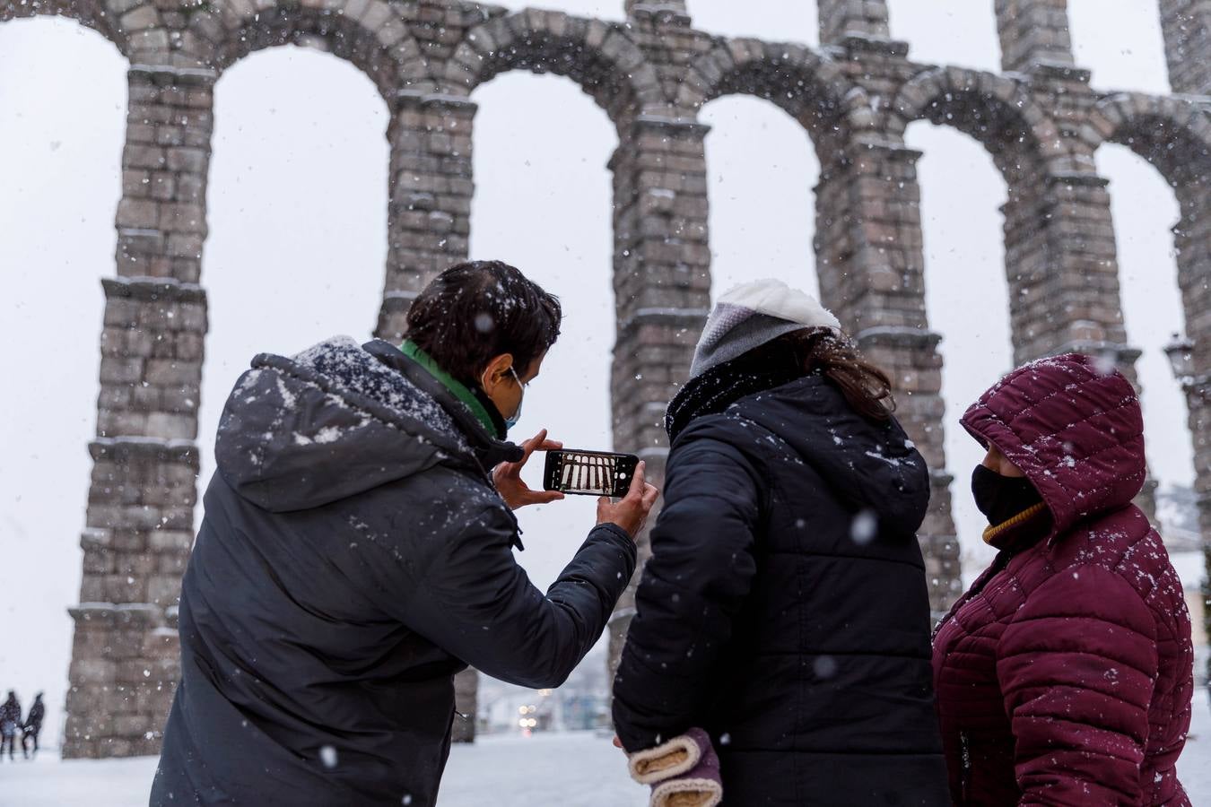 Unos jóvenes fotografían el acueducto de Segovia nevado.