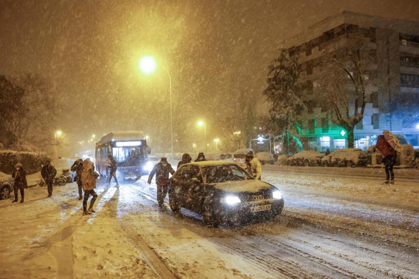 Varias personas empujan un vehículo bajo una intensa nevada en la avenida Ramón y Cajal, en Madrid. 