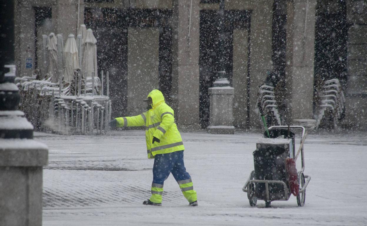 Un operario esparce sale en la jornada de este viernes por la Plaza Mayor, durante la nevada en Segovia. 