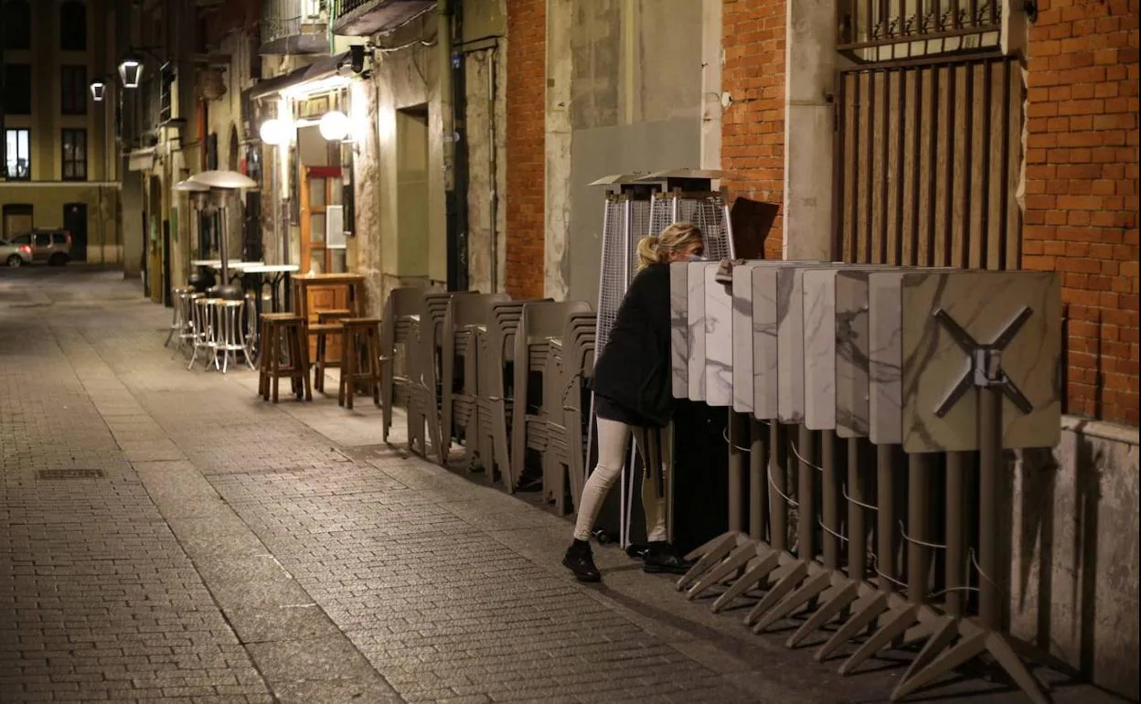 La empleada de un bar de la calle Correos recoge la terraza en la segunda jornada con el toque de queda a las 20:00 horas..