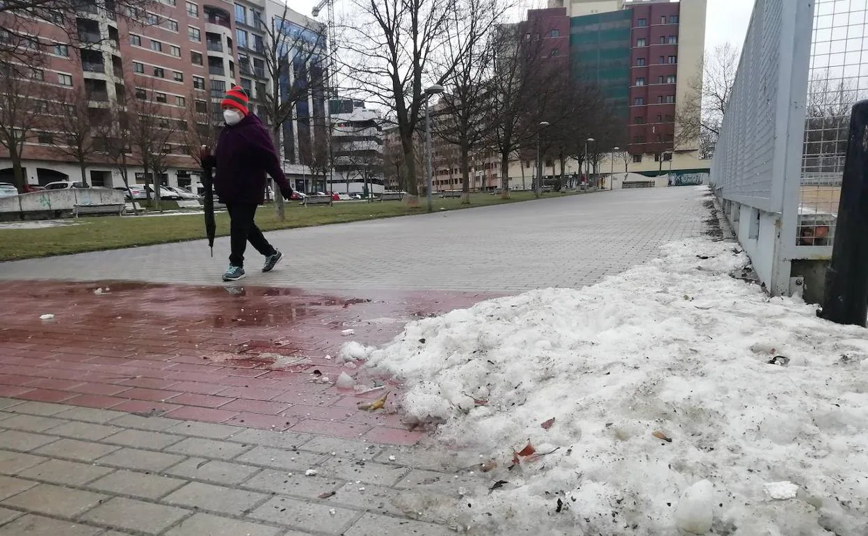 Una mujer pasea con su paraguas en la tarde de ayer ante restos de nieve en Parquesol.
