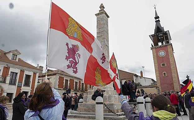 Dos jóvenes hacen ondear la bandera de Castilla y León delante del monolito de Villalar.