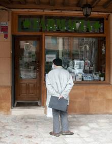 Imagen secundaria 2 - Calle vacía, sin peatones ni vehículos durante la mañana de ayer. El cartero transita por las cercanías del Ayuntamiento. Una persona aguarda su turno para entrar en la farmacia. 