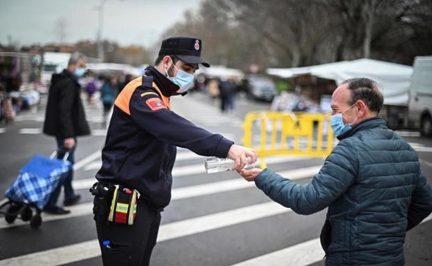 Un agente ofrece gel hidroalcohólico a un hombre a su llegada al mercadillo de Alcalá de Henares (Madrid) 