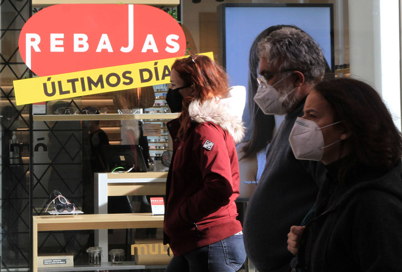 Varias personas pasean por delante de una tienda que anuncia los últimos días de rabajas.