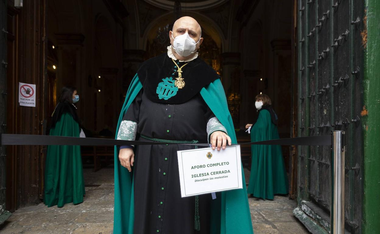 Un cofrade sostiene un cartel de aforo completo debido a las restricciones en la Iglesia de la Vera-Cruz