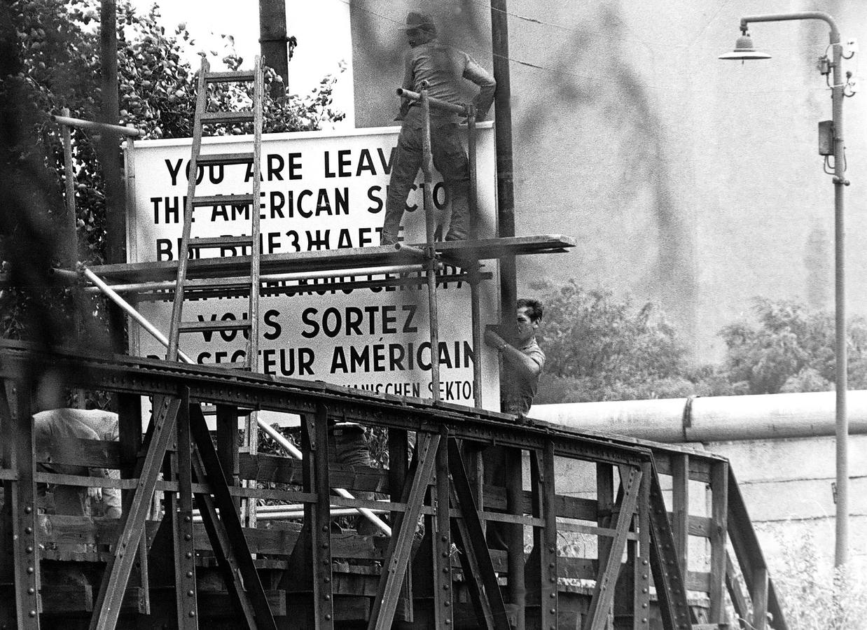 Soldados colocan un cartel en que se advierte a los peatones que deben abandonar el sector americano de Berlín. En segundo término, el Muro.