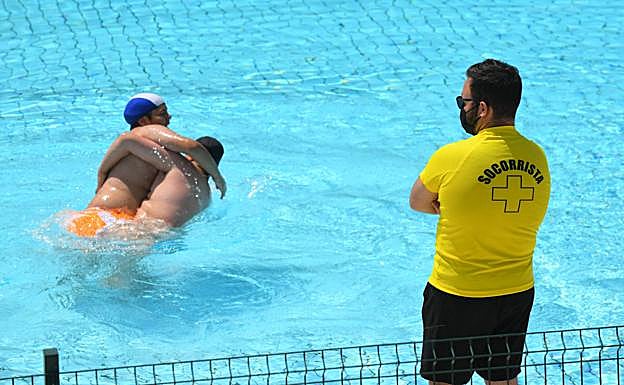 Dos bañistas juegan en el agua bajo la atenta mirada de un socorrista en la piscina de Canterac.
