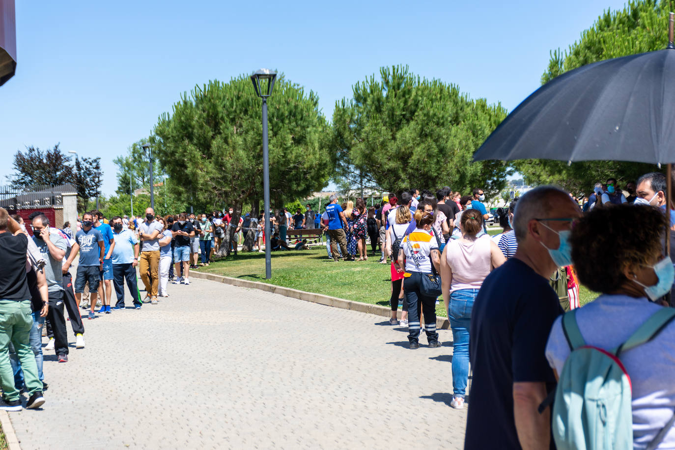 Unos palentinos se protegen del sol bajo un paraguas, el jueves por la tarde, con largas colas para la vacunación en Campos Góticos. 