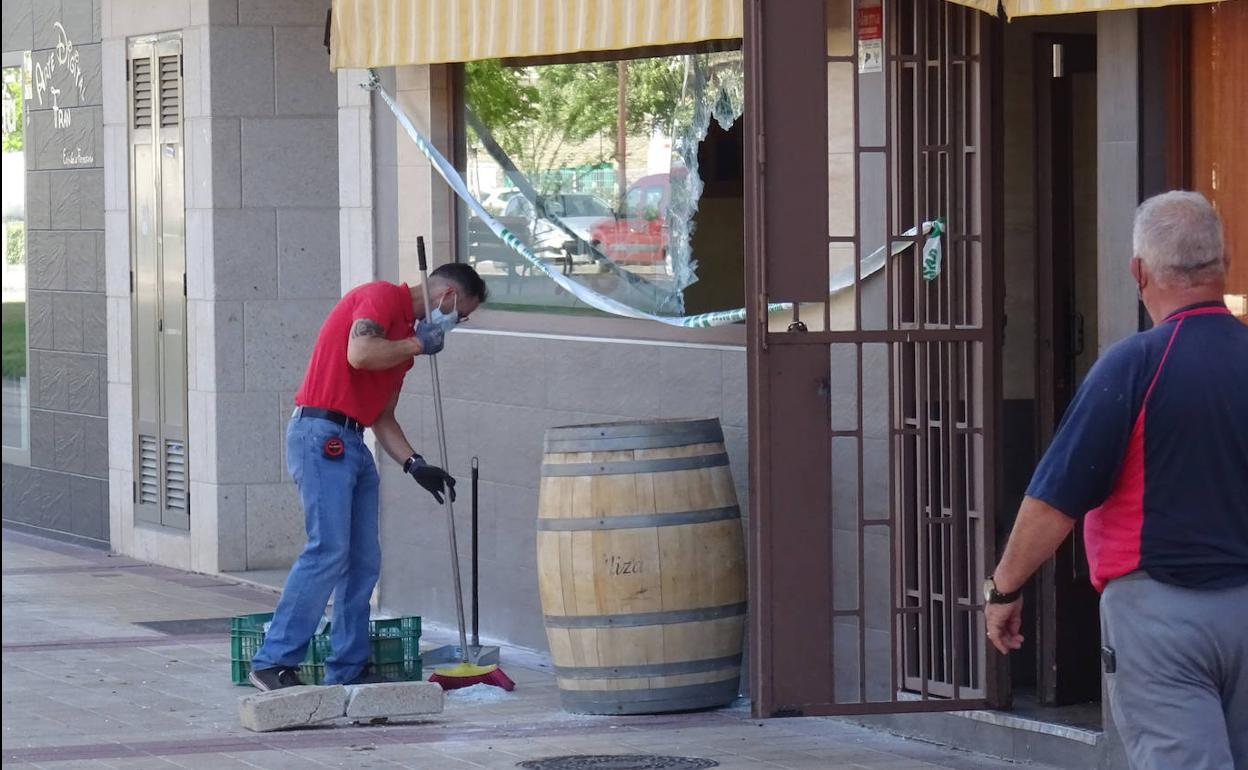 Un operario recoge los cristales rotos de la luna del bar desvalijado en Arroyo. 