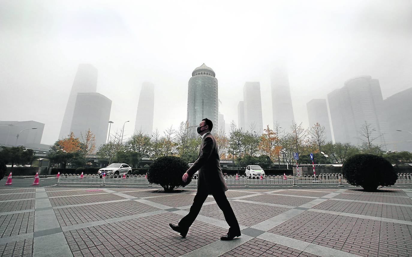 Un hombre camina por las calles de Pekín con la ciudad sumergida en una nube baja de contaminación.