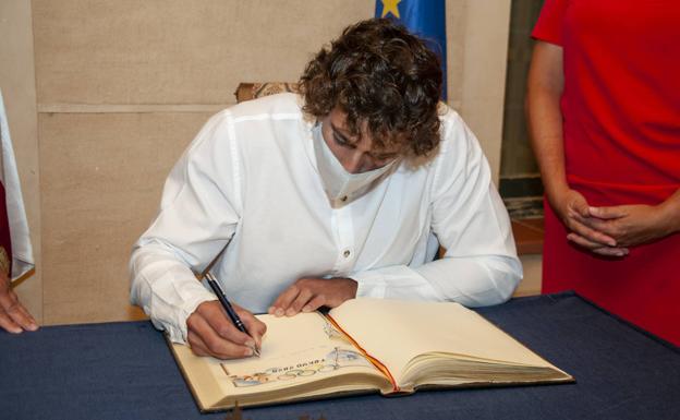 Imagen principal - Arriba, David Llorente firma en el libro de honores de la ciudad de Segovia. Abajo, el piragüista recibe el abrazo de la alcaldesa, Clara Luquero, y la dedicatoria en un apágina especialmente dibujada con motivos de Tokio 2020.