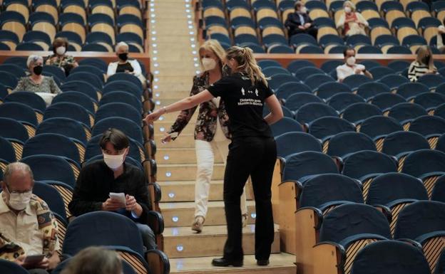 Una azafata indica el lugar donde debe sentarse a una mujer que asiste a un evento cultural. 