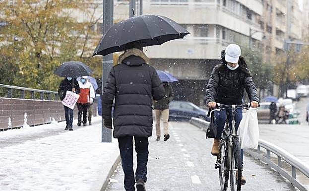 Varias personas pasean hoy bajo la nieve por el puente de Isabel la Católica.