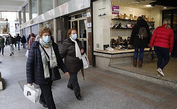 Dos mujeres pasan delante de un escaparate con bolsas. 