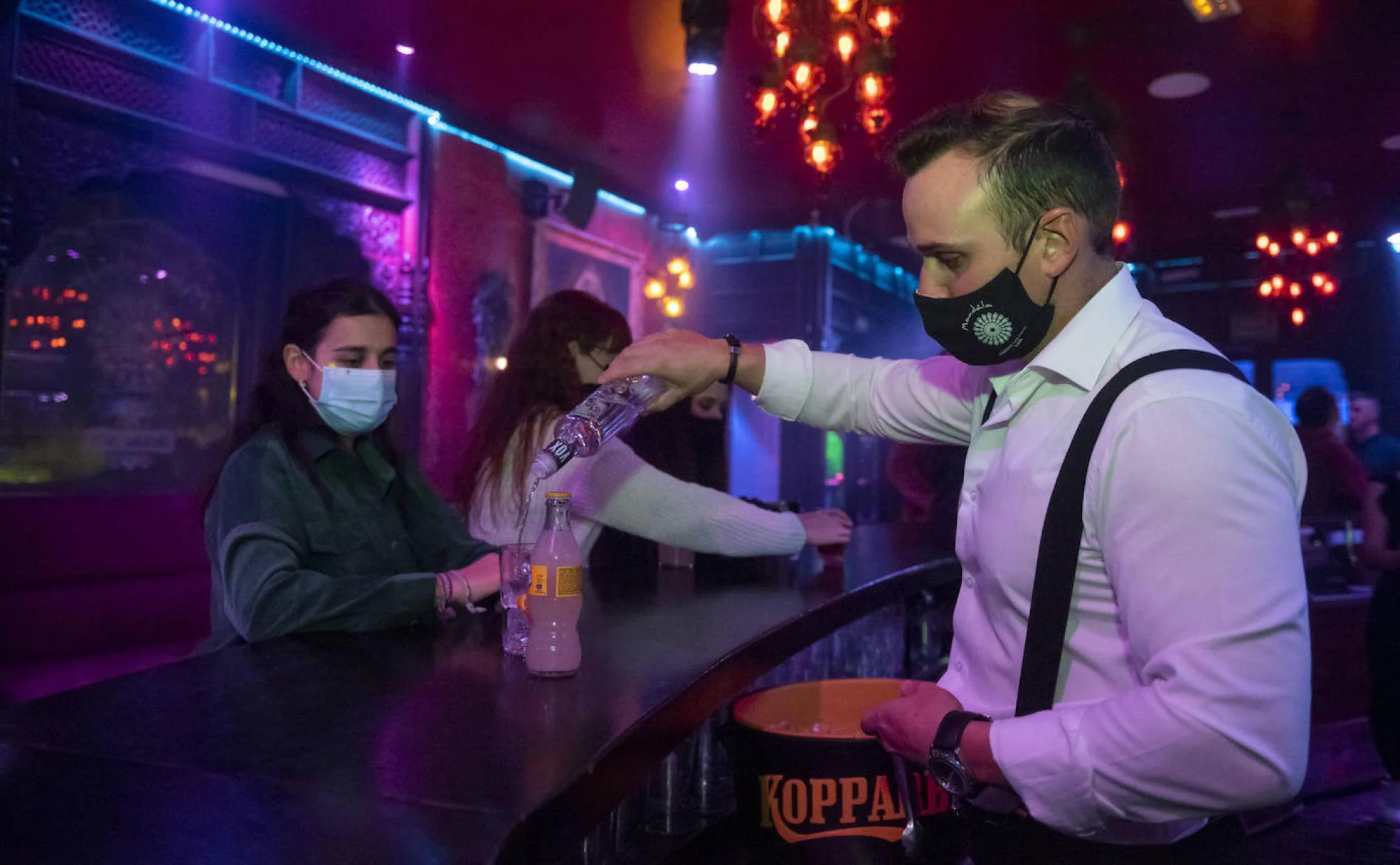 Un camarero de un local de Segovia sirve una bebida a una joven en la barra con mascarilla. 