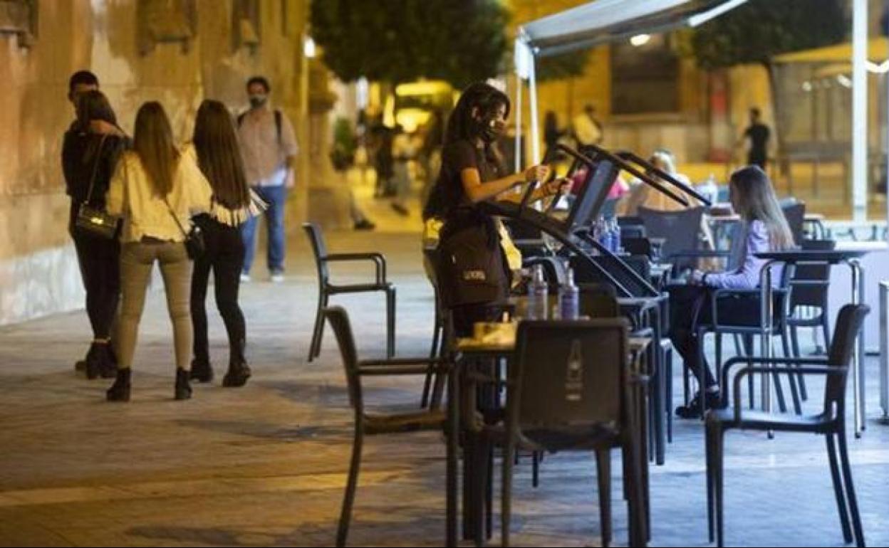 Una joven recoge la terraza de un bar de Murcia. 