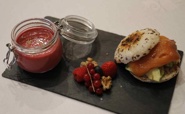 'Smoothie' de frutos rojos. Licuar un plátano, 30 gr de arándanos, 15 gr de moras, 10 de fresas y 200 ml de leche semidesnatada o leche de soja. Decorar con grosellas y semillas de lino. Pan de cereales con un aguacate pequeño, dos lonchas de salmón ahumado y AOVE. 