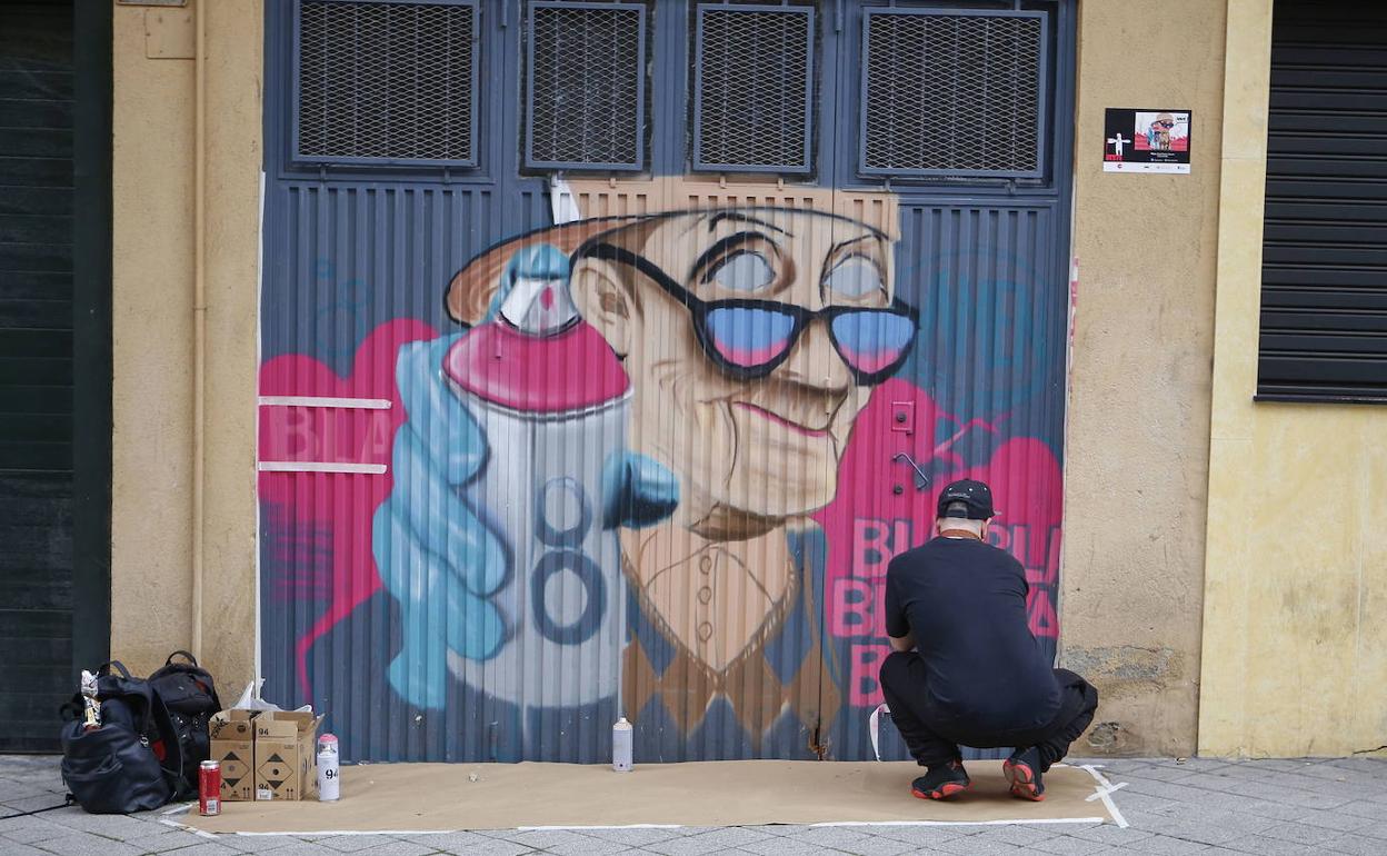 Artista pintando sobre una puerta de un garaje en la VII Galería Urbana del del barrio del Oeste de Salamanca. 