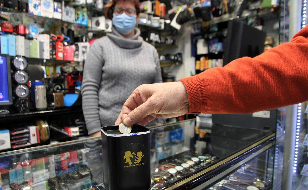 Una persona deposita un euro en la hucha de un establecimiento de la ciudad.