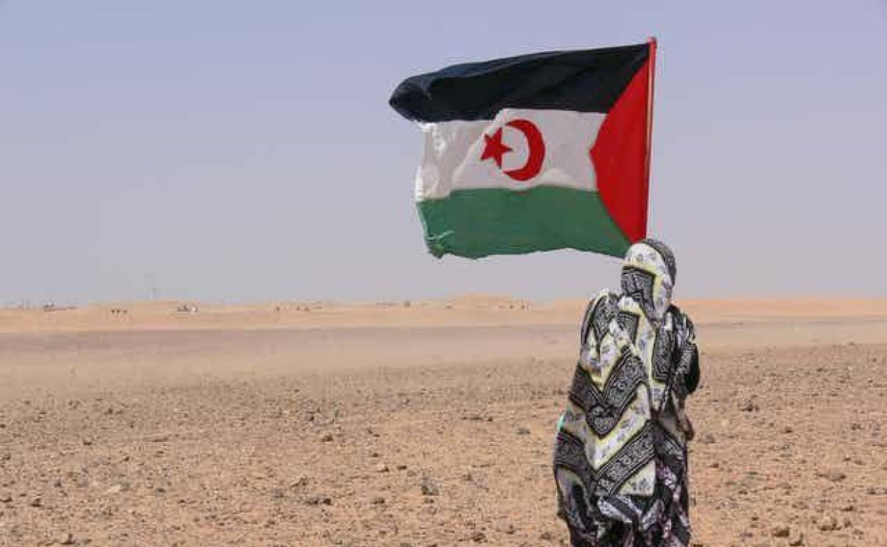 Una persona sostiene una bandera de la República Árabe Saharaui Democrática ante el muro que separa el Sáhara Occidental de Marruecos.