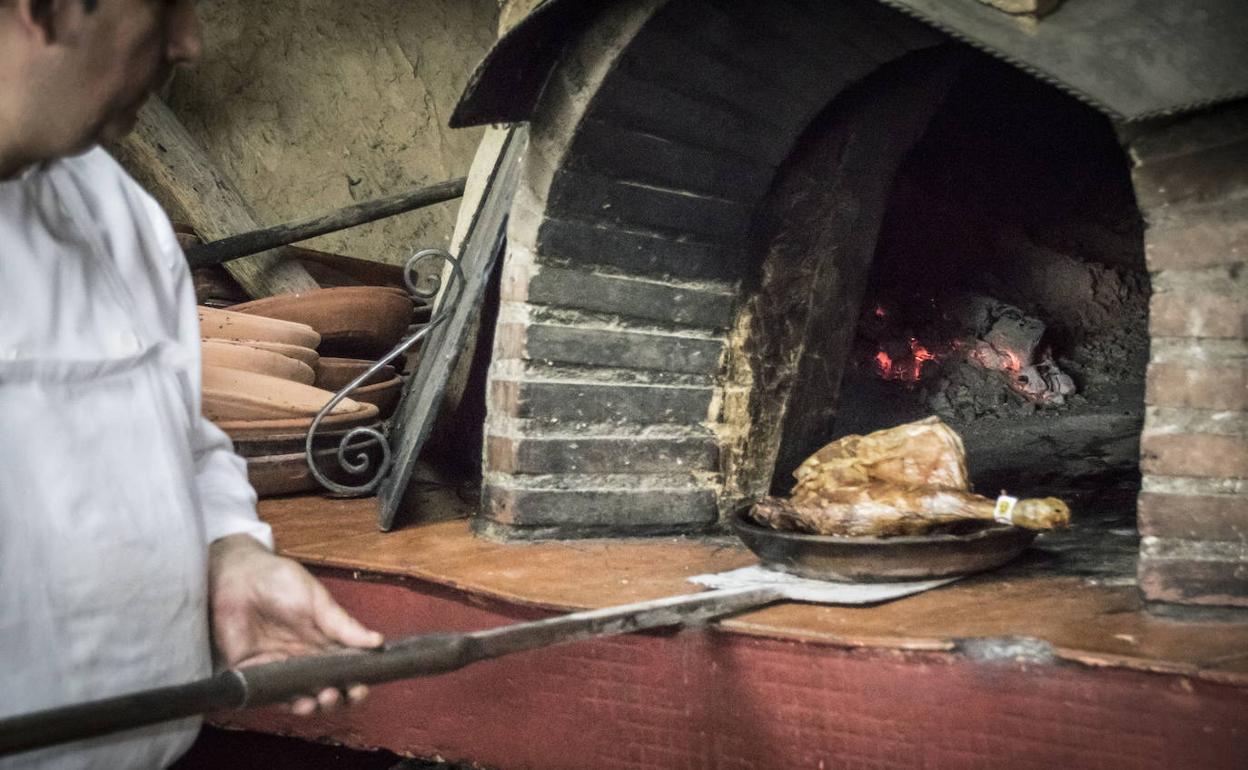 Un cocinero pepara un plato de lechazo en un horno de leña.