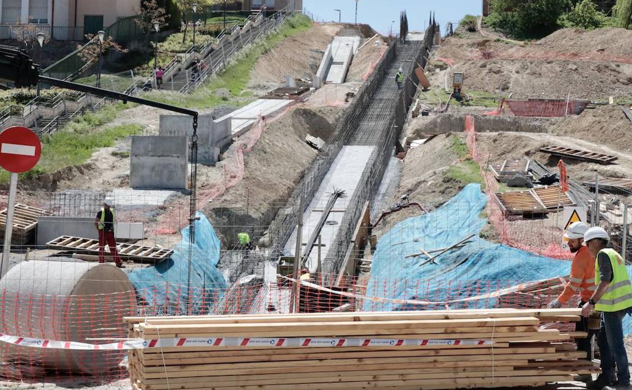 Operarios trabajan en la obra del ascensor y la rampa-escalera mecánica en la ladera que une la piscina con el instituto.