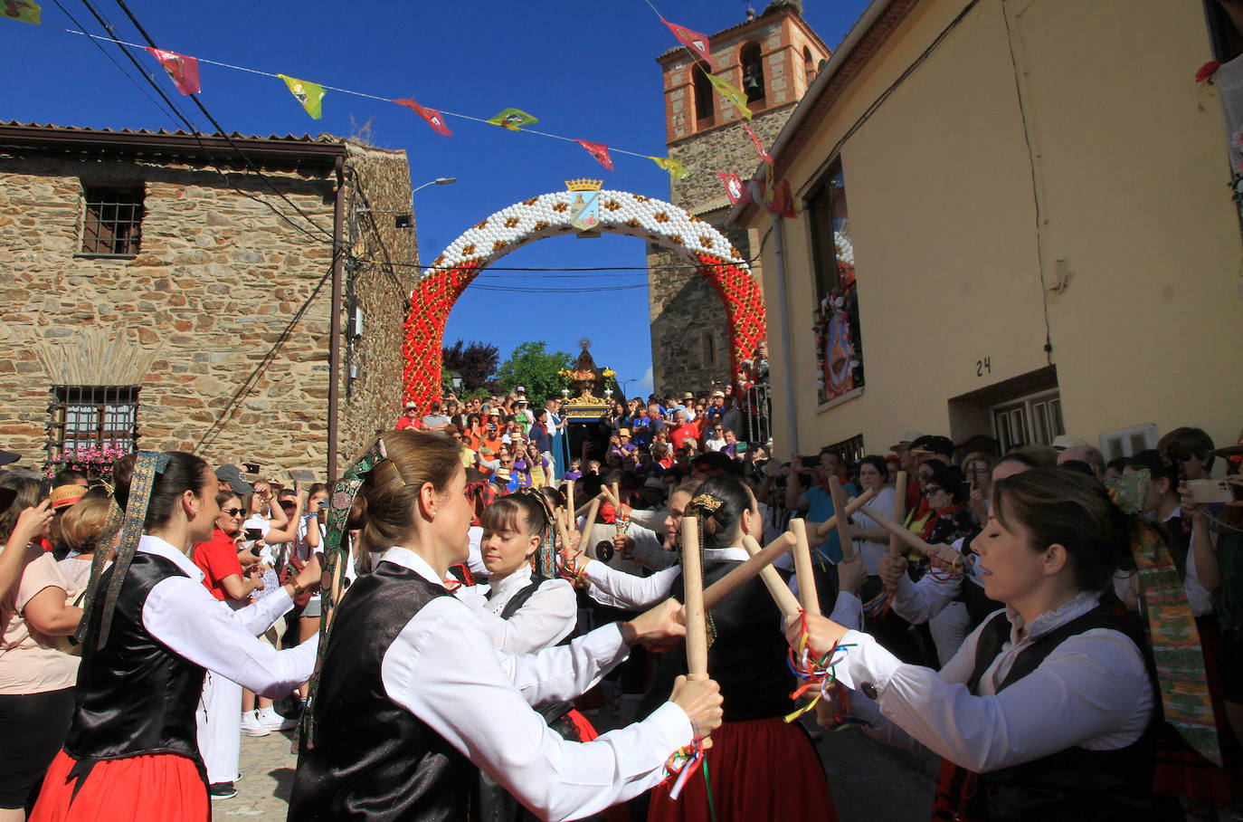 Los grupos de paloteo preceden el paso de la Virgen del Castillo por uno de los arcos de flores de papel en Bernardos. 