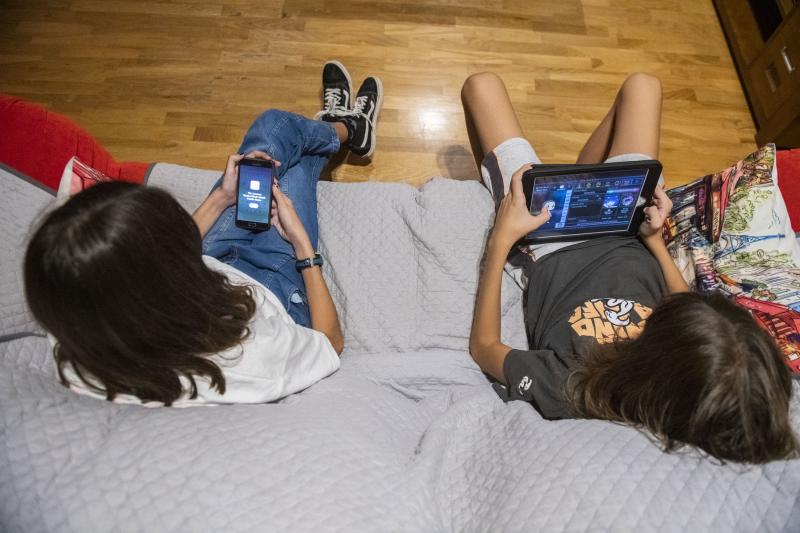 Dos niños juegan con el móvil y la tablet en el salón. 