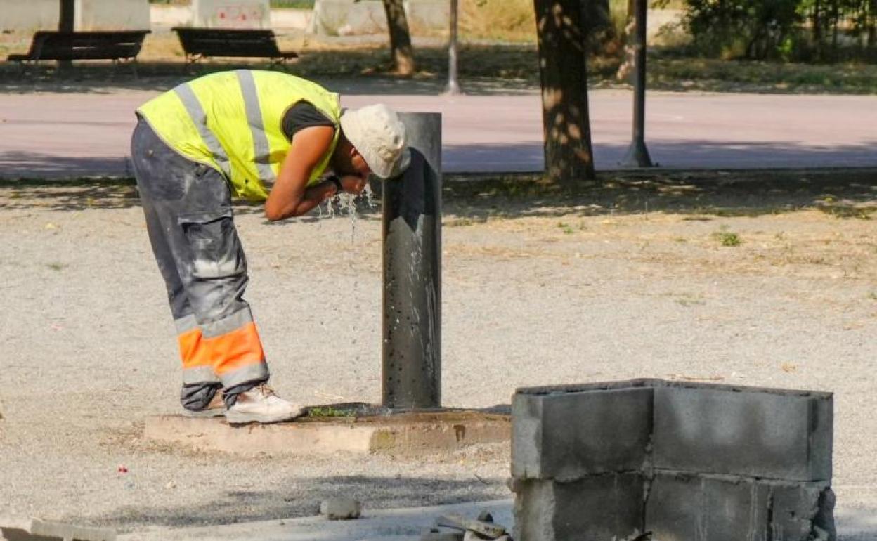 Un trabajador se refresca en un fuente. 