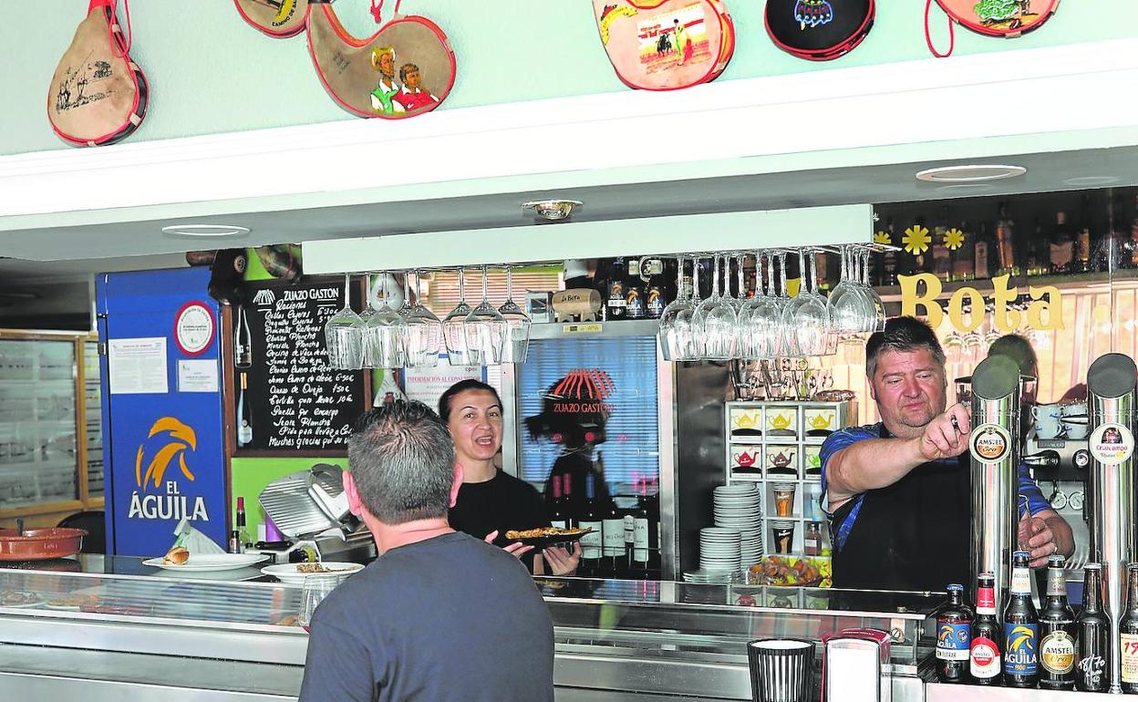 Remi Galiano y Miguel Merino, detrás de la barra del bar La Bota, atienden a un cliente, este lunes.