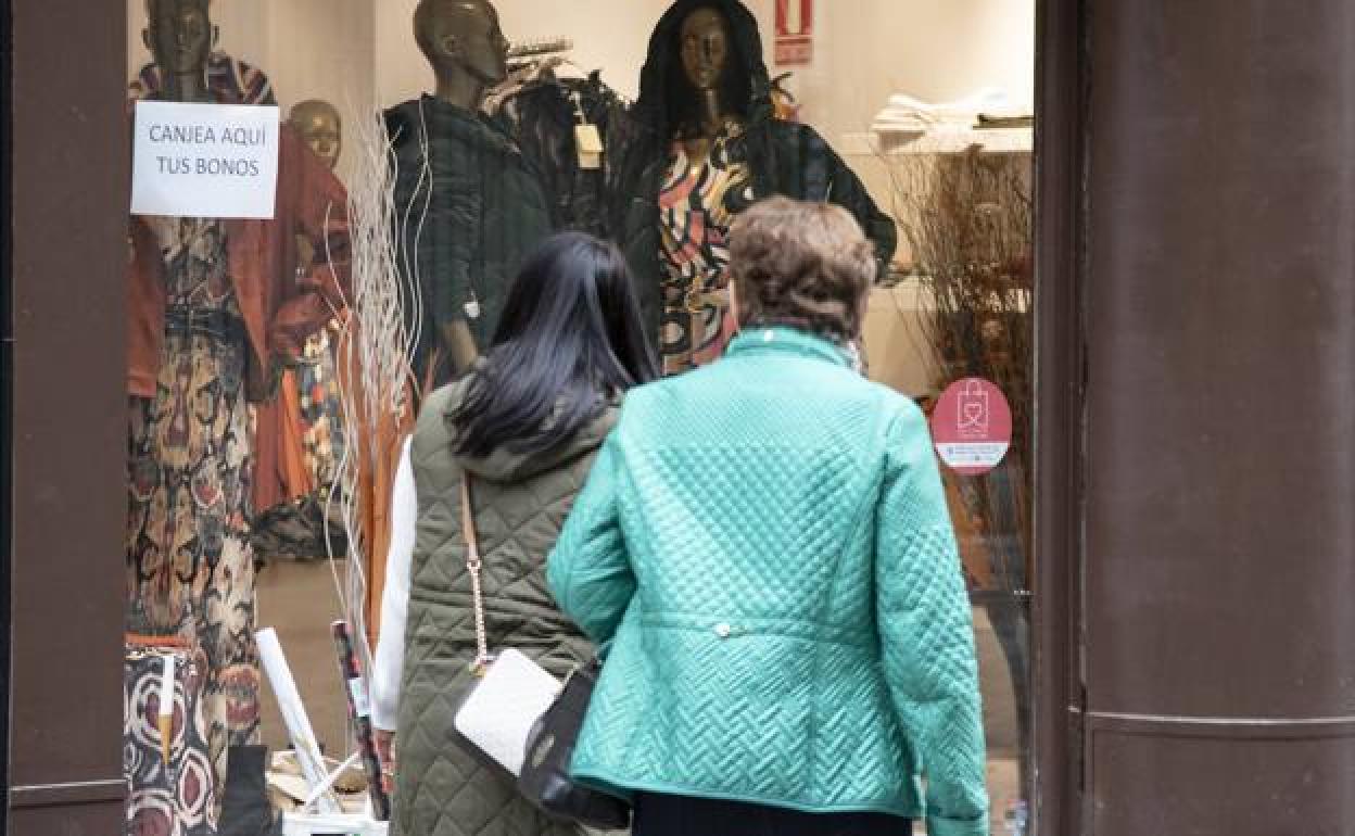 Dos mujeres observan el escaparate de un comercio textil, que permite canjear bonos comercio. 