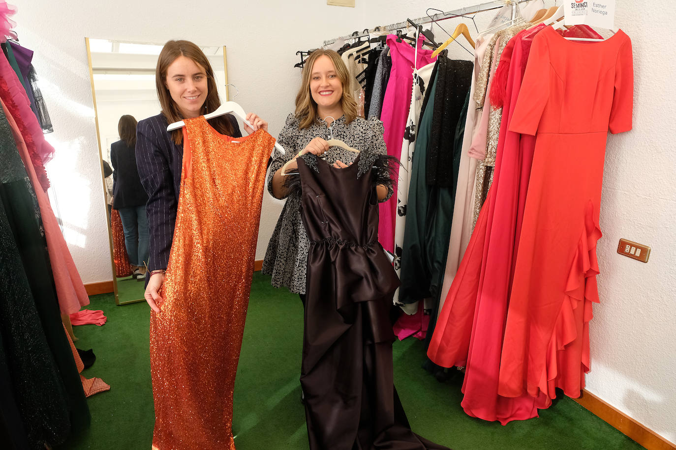 Imagen principal - Mónica Gete y Ainhoa Alonso muestran un vestido naranja de Baro Lucas, uno negro de Alejandro Maillo; a su derecha, un perchero con diseños de Esther Noriega. En la segunda imagen, la coordinadora del 'showroom' se prueba unos zapatos de Hispanitas. En la tercera imagen, Sonia Nieto maquilla a una participante de la Seminci.