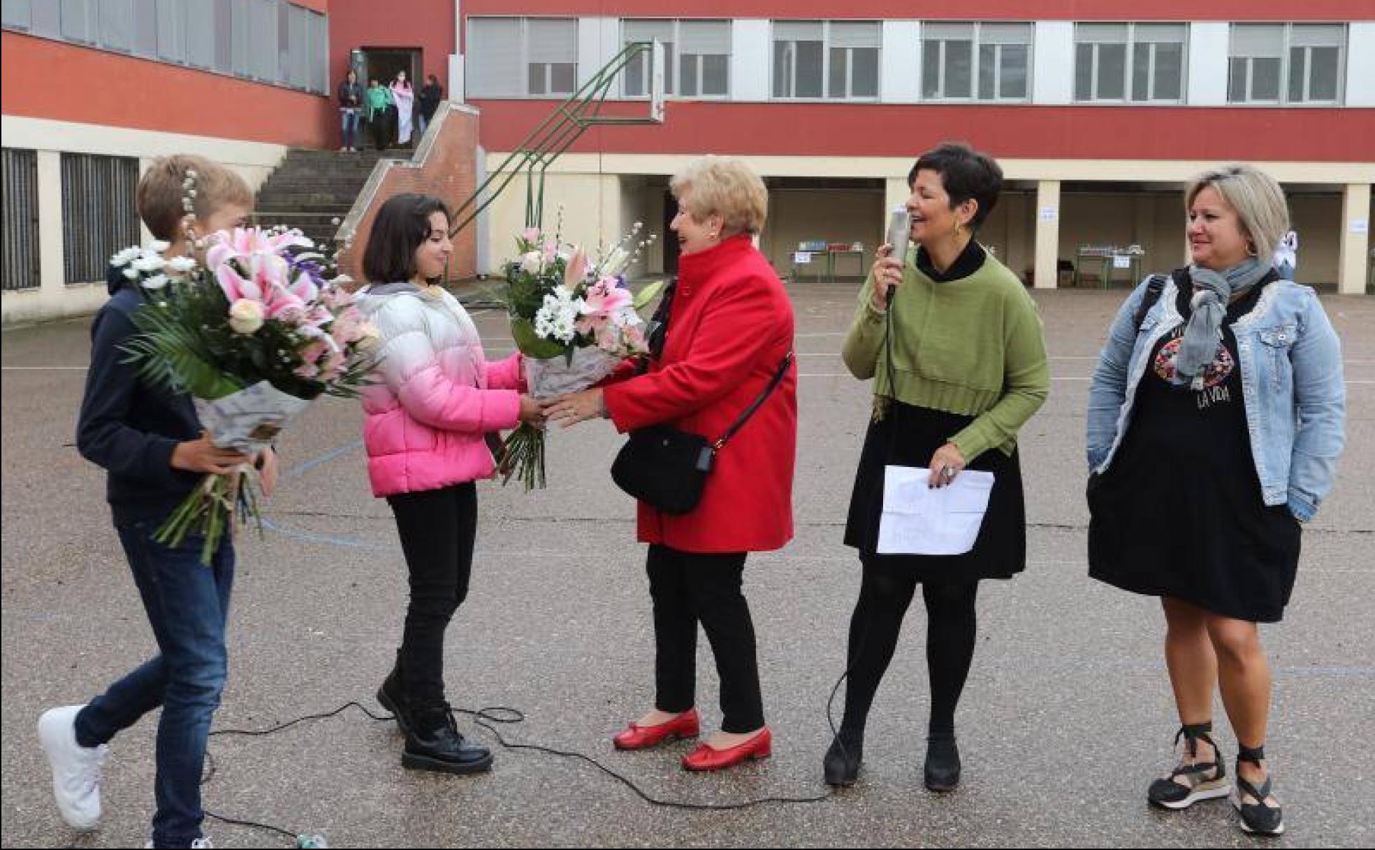 La directora, Asun Alfonso, en el centro, relata al micrófono cómo dos alumnos entregan ramos de flores a la profesora Flor Gago y a la representante de las familias, Arancha Castrillo, a la derecha. 