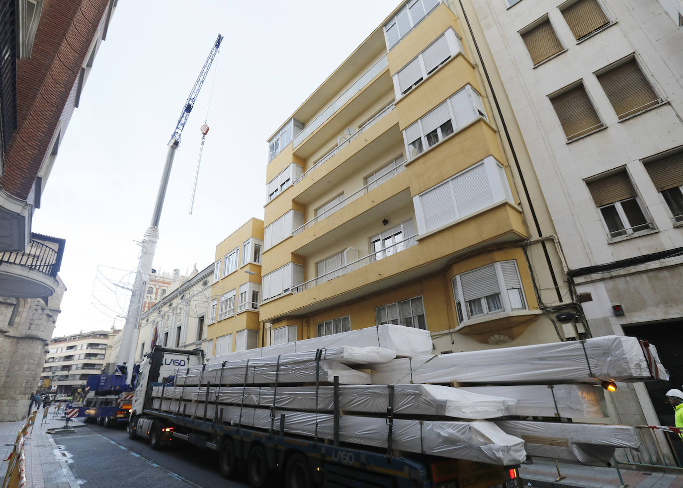 Una grúa de grandes dimensiones trabaja en la calle Burgos para colocar decenas de vigas de madera de tamaño gigante.