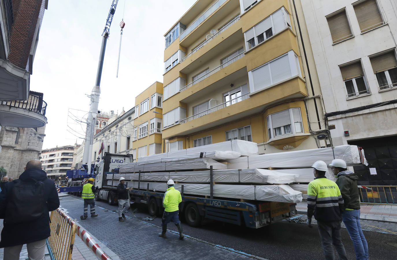 Una grúa de grandes dimensiones trabaja en la calle Burgos para colocar decenas de vigas de madera de tamaño gigante.