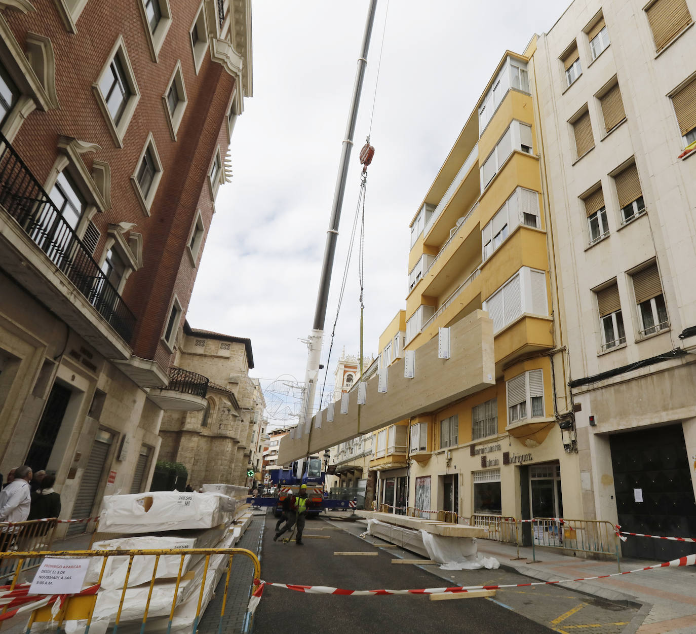 Una grúa de grandes dimensiones trabaja en la calle Burgos para colocar decenas de vigas de madera de tamaño gigante.