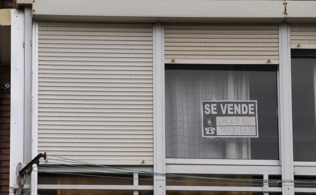 Una ventana con un cartel que anuncia la venta de un piso. 