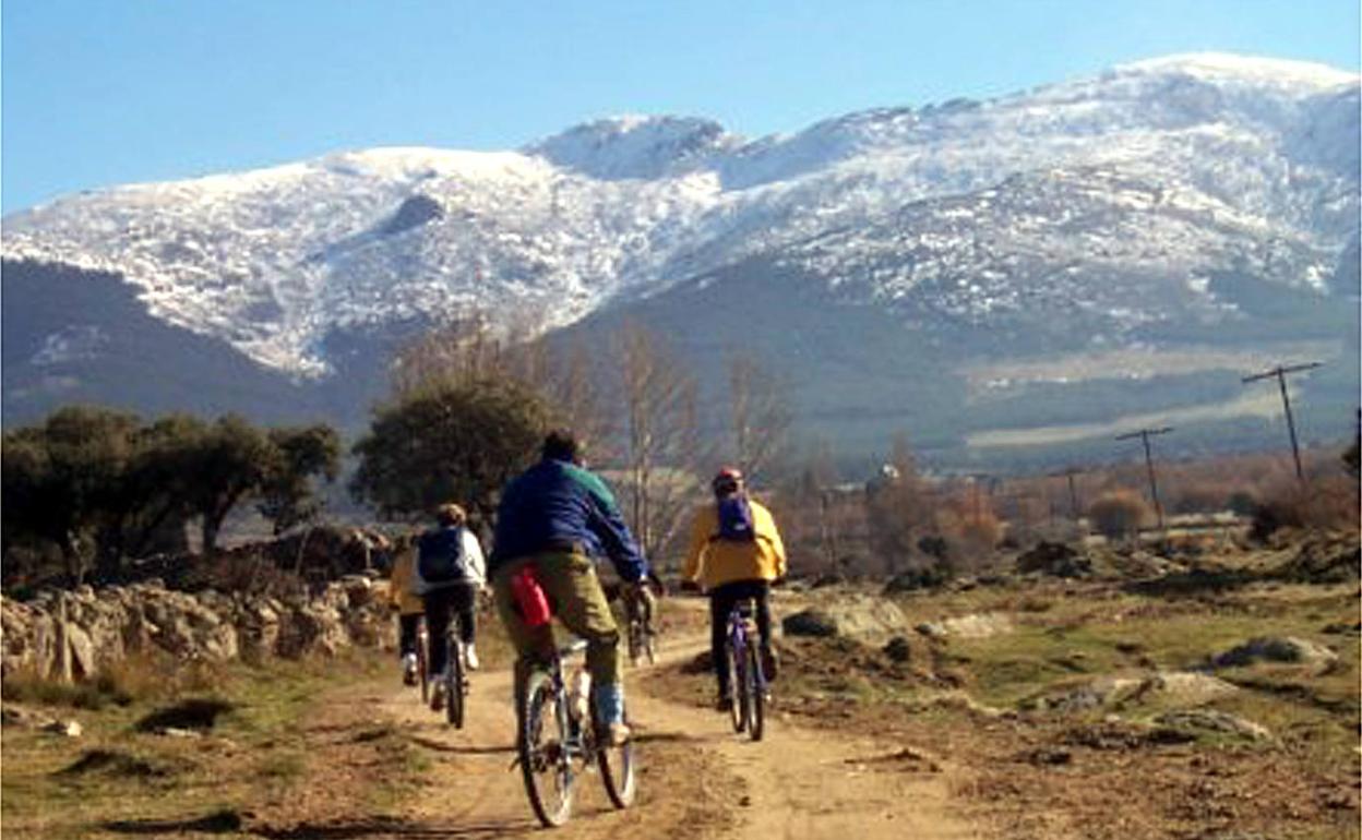 Ciclistas pasean a los pies de la sierra de Guadarrama y con el pico de la Mujer Muerta al fondo. 
