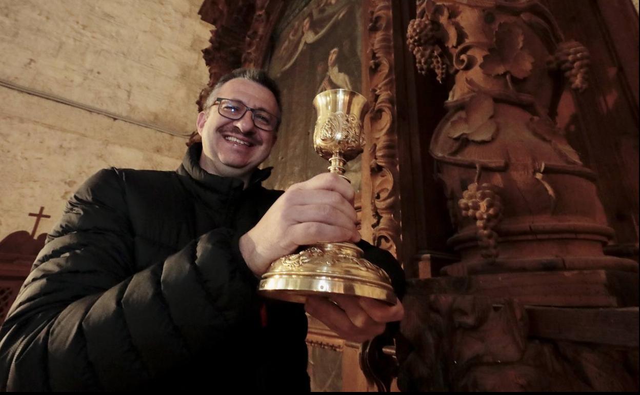 El sacerdote Alfredo Lanchero posa con un cáliz junto a un hermoso retablo con parras y racimos en sus columnas. 