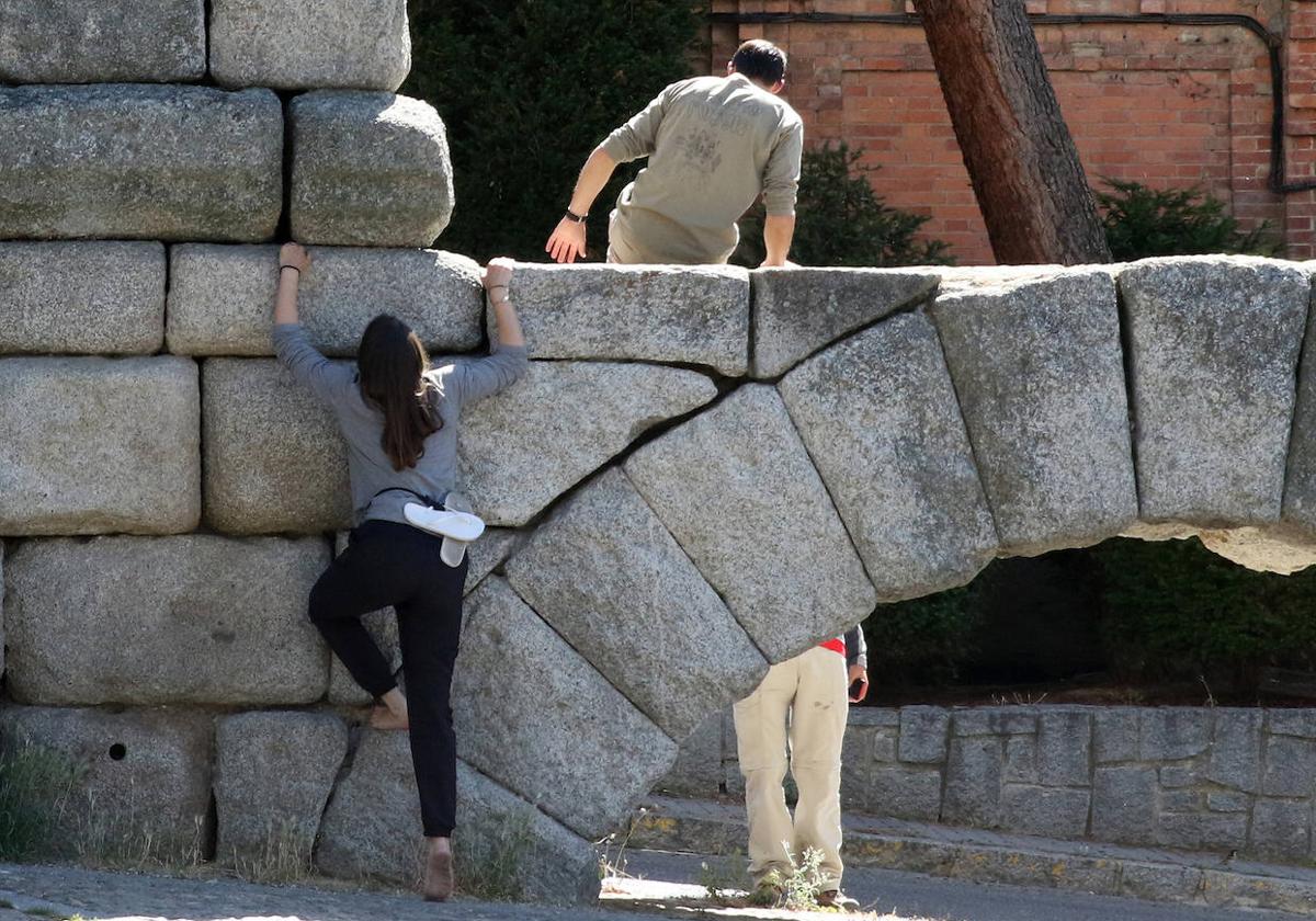 Un hombre, subido al Acueducto mientras una mujer intenta subir por sus sillares, en un foto de archivo.