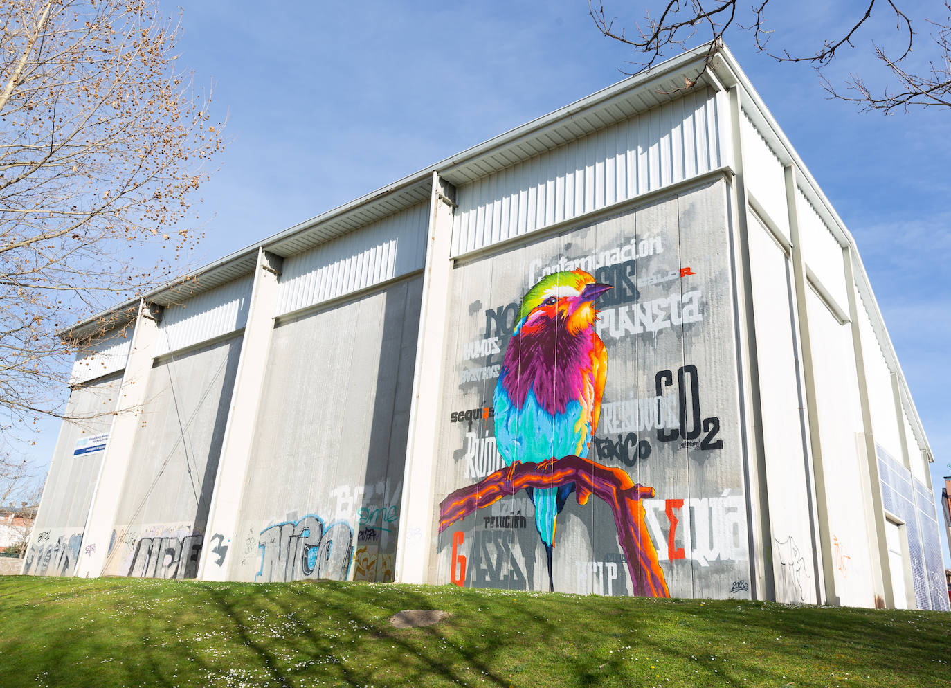 También en el Barrio España, en la calle Valle de Arán, nos topamos con un mural realizado en el frontón Soto de la Medinilla. En él, se contemlpa un pajaro de colores vivos posado sobre la rama de un árbol. Es una denuncia social sobre el cambio climático y el cuidado del planeta, pues en torno al ave se pueden leer palabras como 'contaminación', 'residuos', 'planeta', 'CO2', 'sequía' o 'help', entre otros.