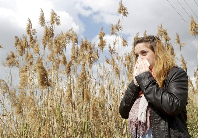 Una mujer estornuda en una zona de vegetación.